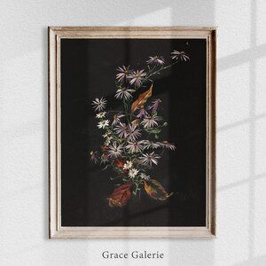 Puede incluir: Impresi&oacute;n floral enmarcada con un ramo de flores moradas y blancas y hojas marrones sobre un fondo negro. La obra de arte est&aacute; en un marco blanco desgastado. El texto "Grace Galerie" est&aacute; en la parte inferior.