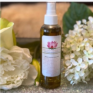 Puede incluir: Una botella de vidrio transparente con un líquido verde en su interior. La botella tiene una tapa de pulverización blanca y una etiqueta blanca con una flor de loto rosa y el texto "Nancy Natural Beauty Skin Care" y "Natural Anti-Itch Scalp Spray". La botella está sobre una superficie brillante.