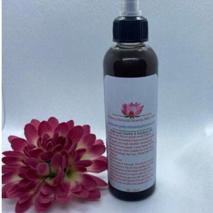 May include: A brown glass bottle with a black cap and a pink flower label. The bottle contains a dark liquid and is labelled "Natural Chebe & Karkar Oil".