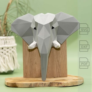 Puede incluir: Una cabeza de elefante de papel gris montada en una base de madera. El modelo está hecho de papel doblado y tiene un diseño geométrico. La base está hecha de madera y tiene un acabado natural. El modelo es una representación 3D de una cabeza de elefante y es un gran ejemplo de papercraft.