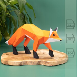 Könnte beinhalten: Ein Papiermodell eines Fuchses, das auf einem Holzsockel steht. Der Fuchs ist aus orangefarbenem und weißem Papier gefertigt und hat eine schwarze Nase und Augen.