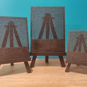 Puede incluir: Tres pequeños caballetes de madera, cada uno mostrando una silueta negra de una familia sobre un fondo de malla marrón.