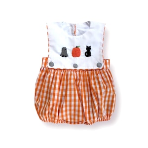 May include: A Halloween-themed baby bubble romper. The white bib features embroidered designs of a ghost, pumpkin, and black cat. The romper has an orange and white gingham pattern. The bib is secured with three black and white checkered buttons.