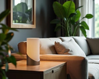 May include: A white table lamp with a ribbed glass shade and a brown metal base sits on a wooden end table in a living room. The lamp is turned on and casting a warm glow.