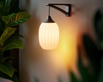 Op de afbeelding: Een witte geribbelde keramische wandlamp met een zwart snoer en een donkerbruine wandbevestiging. De lamp is aan en geeft een warm licht.