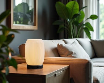 May include: A white ceramic table lamp with a ribbed design sits on a wooden table next to a beige sofa. The lamp is turned on and emits a warm glow.
