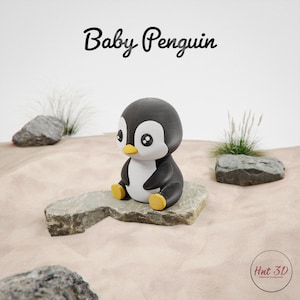 May include: A black and white baby penguin figurine with yellow feet and beak, sitting on a gray rock. The text "Baby Penguin" is above the penguin. The background is a sandy texture with rocks and grass.