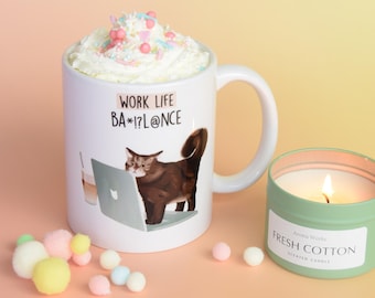May include: White ceramic mug with a brown cat looking at a laptop and the text "Work Life BA*!@L@NCE". The mug is filled with white whipped cream and colourful sprinkles. A green candle with the text "Fresh Cotton Scented Candle" is in the background.
