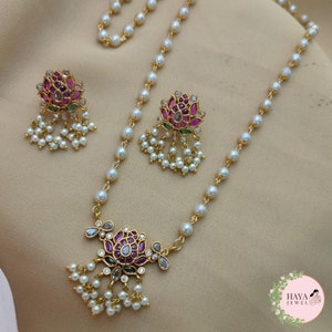 Peut inclure: Un collier en or avec un pendentif en forme de lotus rose et vert et des gouttes de perles. Le collier est assorti à des boucles d'oreilles.