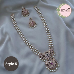May include: A three-strand pearl necklace with a gold pendant featuring intricate floral designs and pink and green gemstones. The pendant is adorned with white pearls. The necklace is accompanied by matching earrings with similar designs.