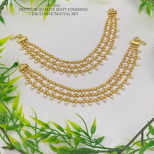 Puede incluir: Un par de pendientes de tono dorado con detalles de perlas blancas. Los pendientes están hechos de múltiples hileras de cuentas y tienen un acabado mate. Los pendientes están etiquetados como "KC 305 PREMIUM QUALITY MATT FINISHING <<EXCLUSIVE>> MATTAL SET".