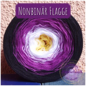 Könnte beinhalten: Nahaufnahme einer Wollknäuel mit schwarzen, violetten, weißen und gelben Streifen. Die Wolle ist mit "Nonbinär Flagge" beschriftet, was im Deutschen "Non-binäre Flagge" bedeutet.