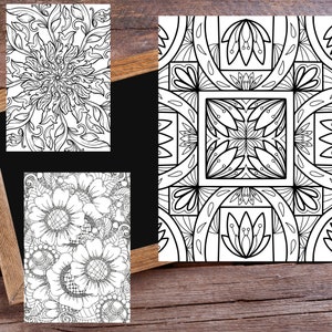 May include: Three black and white coloring pages featuring intricate floral and geometric designs. The pages are displayed on a wooden surface.