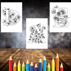 May include: Three printable coloring pages featuring the letters D, A, and E decorated with floral designs. The letters are outlined in black and the flowers are detailed with intricate lines.