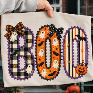 May include: A light-colored fabric panel featuring the word BOO appliqued in large letters. The B is black and white buffalo plaid, the O is orange with ghosts and bats, and the second O has orange and black stripes with a pumpkin.