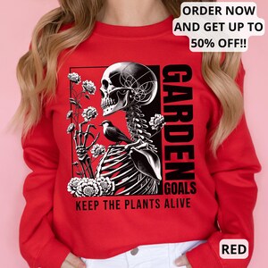 May include: Red sweatshirt with a black and white graphic of a skeleton holding flowers and a bird. The text "GARDEN GOALS KEEP THE PLANTS ALIVE" is printed on the sweatshirt.