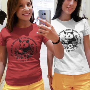 May include: Two women wearing red and white t-shirts with a graphic of an opossum drinking coffee and the text "Life is better with opossums and coffee". They are both wearing yellow shorts.