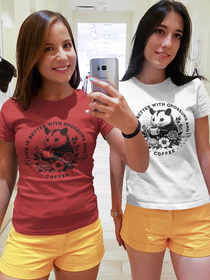 May include: Two women wearing red and white t-shirts with a graphic of an opossum drinking coffee and the text "Life is better with opossums and coffee". They are both wearing yellow shorts.