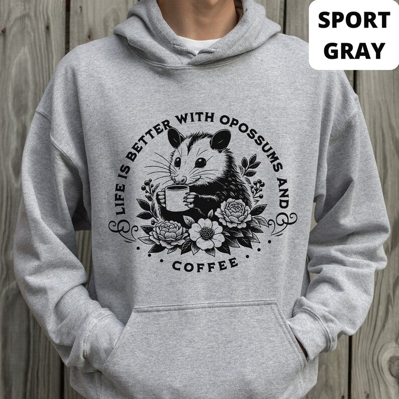 May include: A gray hooded sweatshirt with a black and white graphic of an opossum holding a cup of coffee. The graphic says "Life is better with opossums and coffee".