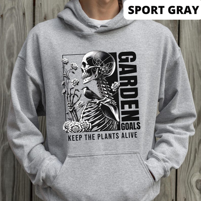 May include: A gray hooded sweatshirt with a black and white graphic print of a skeleton holding flowers and a bird. The text "GARDEN GOALS KEEP THE PLANTS ALIVE" is printed below the graphic. The sweatshirt is labeled "SPORT GRAY".