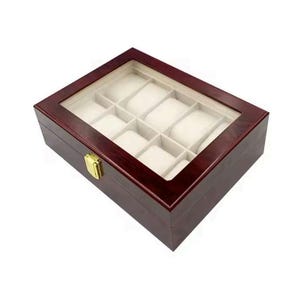 Puede incluir: Una caja de madera de color rojo oscuro para relojes con tapa de cristal transparente y 10 compartimentos forrados de terciopelo blanco. La caja tiene un cierre dorado.