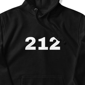 Puede incluir: Sudadera con capucha negra con el número "212" impreso en blanco en la parte delantera.