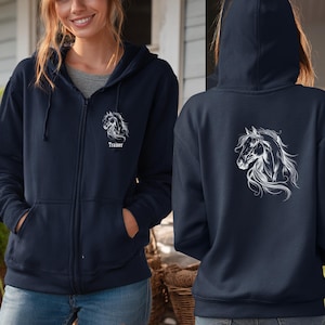 Puede incluir: Sudadera con capucha azul marino con cremallera y un diseño de cabeza de caballo blanco en la parte delantera y trasera. La parte delantera de la sudadera tiene la palabra "Trainer" debajo del gráfico del caballo. La sudadera tiene capucha con cordón y bolsillos delanteros.