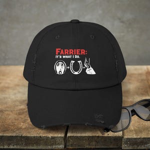 May include: Black distressed baseball cap with white text that reads "Farrier: It's what I do."  The text is accompanied by a horseshoe and a horse's hoof.