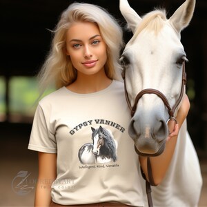 Könnte beinhalten: Eine Frau trägt ein beiges T-Shirt mit einem Motiv eines Gypsy Vanner Pferdes. Der Text auf dem Shirt lautet "Gypsy Vanner" und "Intelligent. Kind. Versatile."