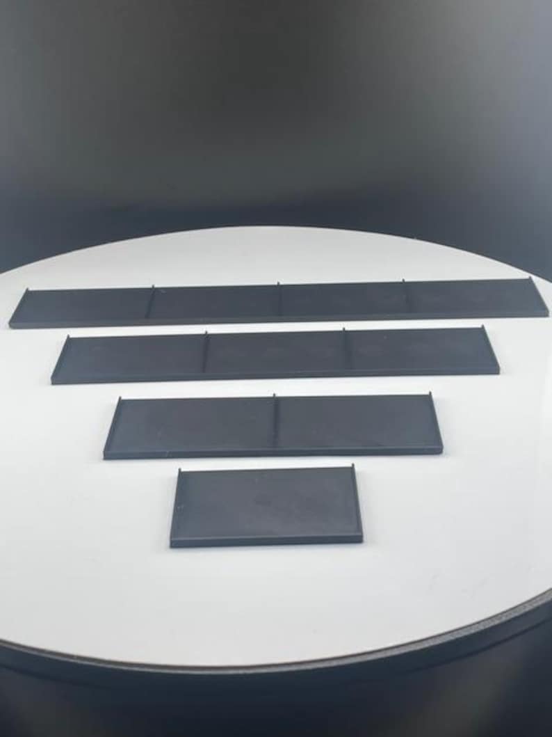 May include: Four black rectangular shelves of varying sizes are arranged on a white surface. The shelves are made of a matte material and have a simple, minimalist design. The shelves are likely for organizing or displaying items.
