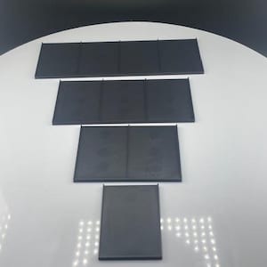 May include: Four black rectangular panels of varying sizes are arranged on a white surface. The panels appear to be made of a matte material and are evenly spaced, creating a tiered effect. The background is a gradient of white to black.