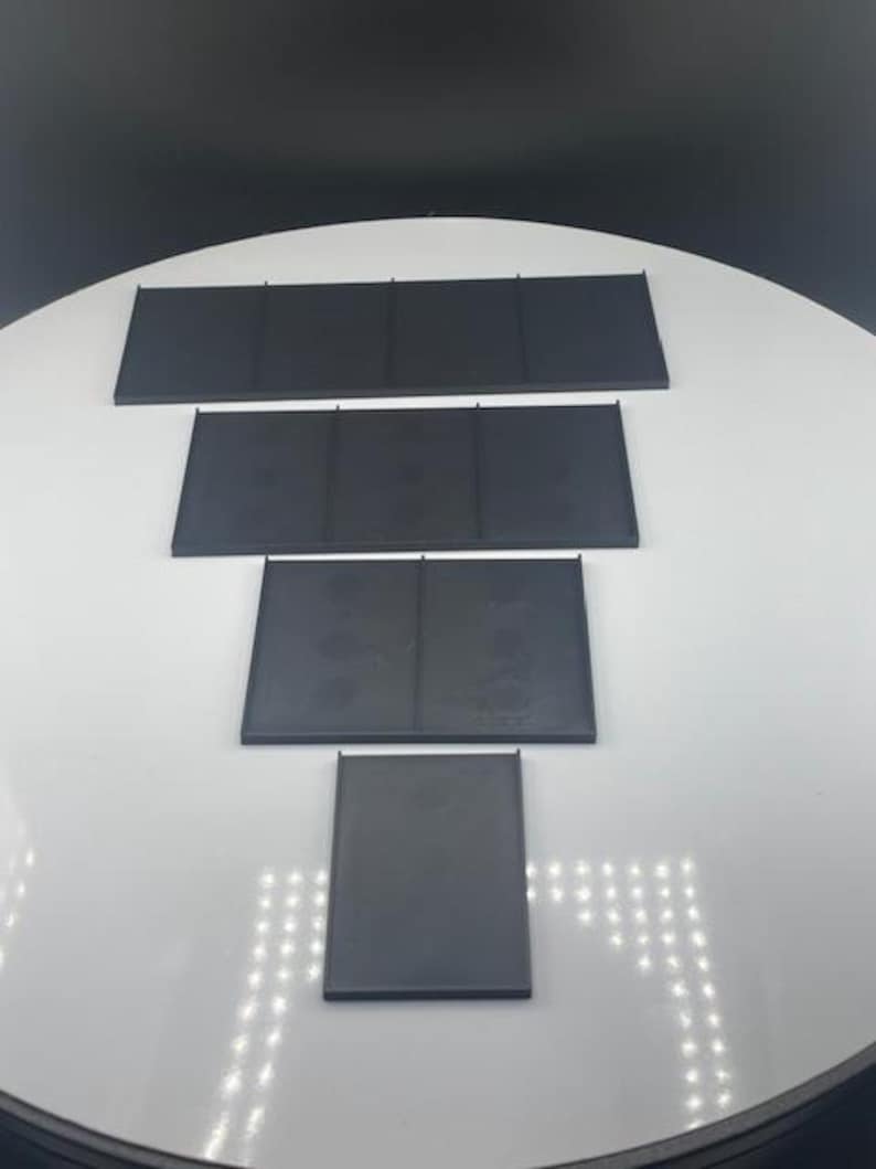 May include: Four black rectangular panels of varying sizes are arranged on a white surface. The panels appear to be made of a matte material and are evenly spaced, creating a tiered effect. The background is a gradient of white to black.