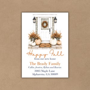 May include: A rectangular card featuring a white front door with a wreath, flanked by lanterns and pumpkins. Text reads: Happy Fall from our new home, The Brady Family, Collin, Jessica, Rylan and Rowan, 3003 Maple Lane, Alpharetta, GA 30009.