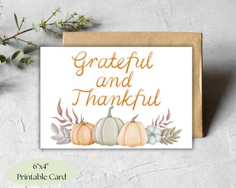 May include: Printable card with the text "Grateful and Thankful" in orange lettering. The card features a watercolor illustration of three pumpkins with fall leaves and a white flower.
