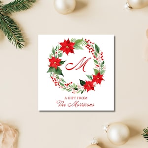 May include: A white gift tag with a red poinsettia wreath and the letter "M" in the center. The text "A gift from The Morrisons" is at the bottom of the tag.