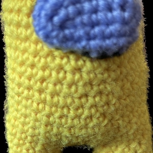 May include: A yellow crocheted plush toy shaped like the character from the video game Among Us. The toy has a blue crocheted visor.
