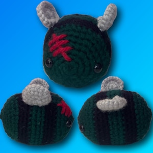 Può includere: Tre peluche di api all'uncinetto con strisce nere e verdi. Un'ape ha un "*" rosso sulla testa e due hanno ali grigie.