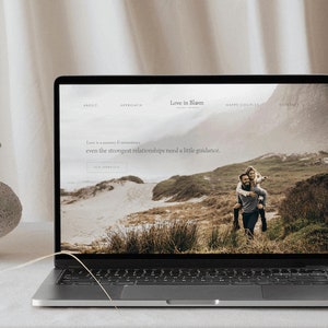 May include: A laptop computer displaying a website for a couples therapist. The website is titled "Love in Bloom" and features a photo of a couple walking on a beach. The text on the website reads "Love is a journey & sometimes even the strongest relationships need a little guidance."