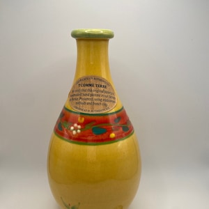 May include: A yellow ceramic vase with a green top and a red, orange, and green floral design. The vase has a label that reads "Tcomme Terre" and "Certificate of Authenticity".