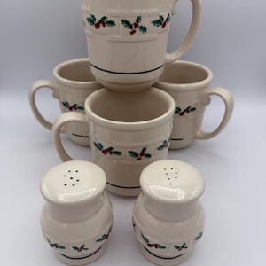 May include: A set of cream-colored ceramic mugs and salt and pepper shakers. The mugs and shakers have a basket weave design with green holly leaves and red berries. Each mug has a black stripe near the base. The salt and pepper shakers have a similar design.