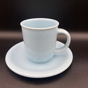 May include: A light blue ceramic teacup and saucer set. The cup has a rounded handle and the saucer is slightly oval shaped.