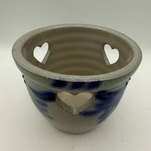 May include: A ceramic bowl with a speckled, light gray exterior and a blue floral design. The bowl features heart-shaped cutouts and a textured interior. The rim is a darker gray.
