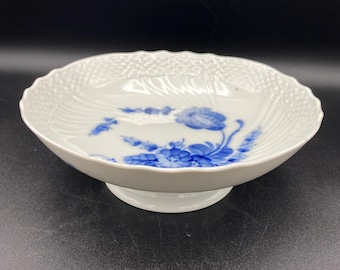 May include: A white porcelain pedestal bowl with a blue floral design. The bowl has a scalloped edge and a raised, textured base.