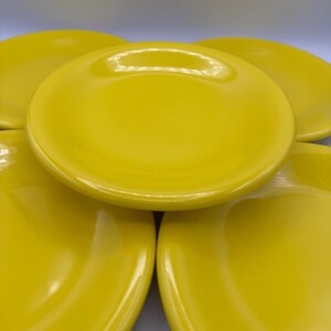 May include: A stack of bright yellow ceramic plates. The plates are round with a slightly raised edge and a glossy finish. The plates are a solid, vibrant yellow color.