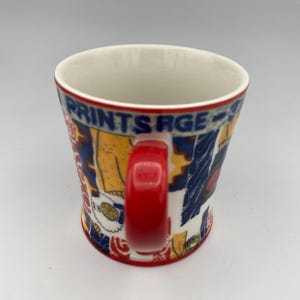 K&ouml;nnte beinhalten: Eine wei&szlig;e Keramiktasse mit einem roten Henkel. Die Tasse hat ein buntes Design mit den Worten "Prints R'age" an der Seite.