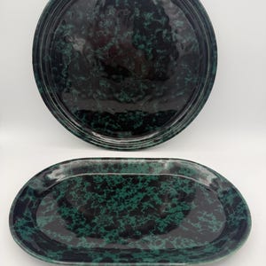 May include: Two ceramic dishes featuring a glossy finish with a dark black and deep green mottled pattern. One dish is circular with a raised rim, while the other is oval-shaped with a smooth, slightly undulating surface texture throughout.