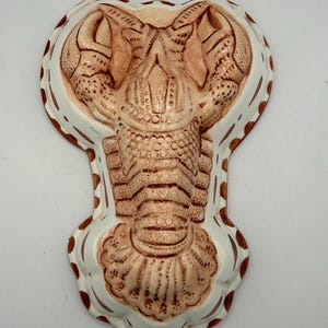 May include: A ceramic cobra-shaped dish with a detailed, textured design. The dish features a cream-colored base with a brown cobra head and body, and a white border with brown polka dots.