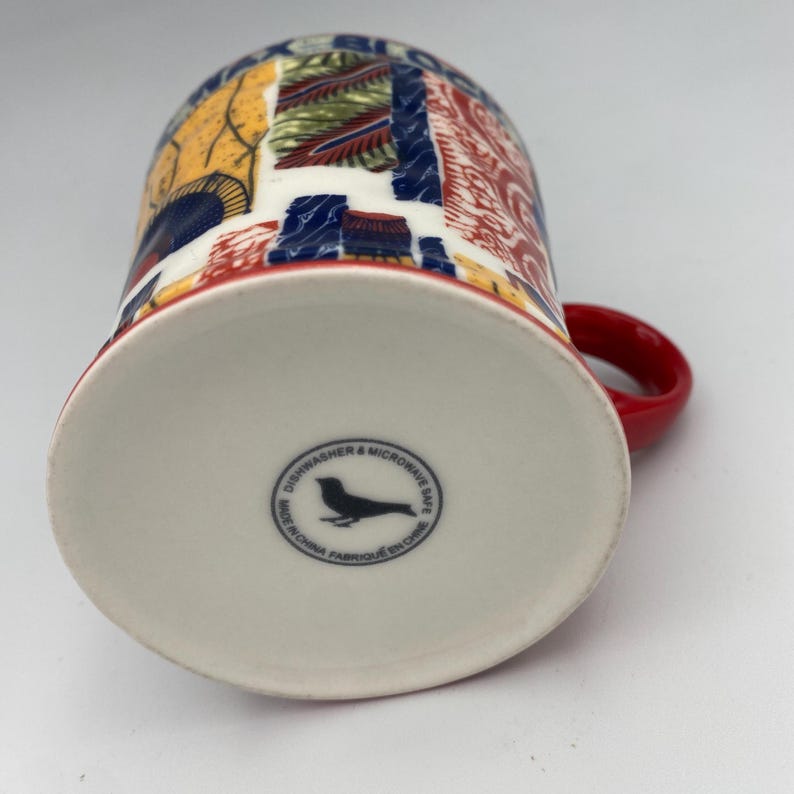 K&ouml;nnte beinhalten: Eine wei&szlig;e Keramiktasse mit rotem Henkel. Die Tasse hat ein farbenfrohes, abstraktes Design in Rot, Blau, Gelb und Gr&uuml;n. Auf der Unterseite der Tasse befindet sich ein schwarzes Vogellogo und der Text "Dishwasher & Microwave Safe. Made in China. Fabriqu&eacute; en Chine."