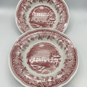 May include: Two pink and white ceramic soup bowls with a winter scene design. The bowls have a scalloped edge and a floral pattern around the rim.