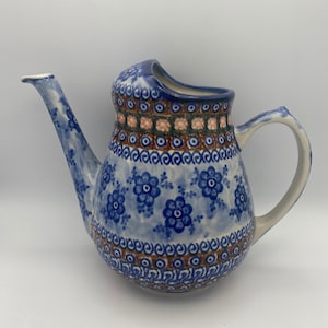 May include: A blue and white ceramic watering can with a floral pattern. The handle is on the right side and the spout is on the left. The can has a wide opening at the top.
